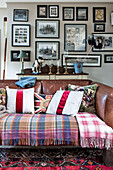 Cushions and blankets on brown leather sofa below framed artwork in Stamford home Lincolnshire England UK