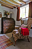 Wingback armchair and wooden writing desk at window of Cambridge cottage England UK