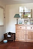 Green lamp on wooden sideboard with dog basket in hallway of Edworth cottage Bedfordshire England UK