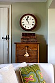 Uhr über altem Holzschrank und Sofa mit Kissen in Edworth-Wohnzimmer Bedfordshire England UK