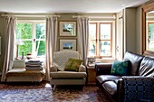 Cream armchair with brown leather sofa in living room of Edworth cottage Bedfordshire England UK