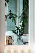 Spruce sprig and cone garlands hang in window with lit candles