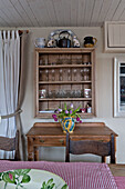 Wineglasses in cabinet above cut tulips on wooden side table in beach house Cornwall England UK