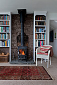 Bookshelves and lit burning stove in beach house Cornwall England UK