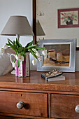 White tulips and paperback book on wooden chest of drawers in beach house Cornwall England UK