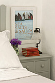 Red hardback books with vintage lamp and poster at bedside in Penzance farmhouse Cornwall England UK