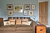Artwork display over brown sofa with cushions in living room of holiday cottage Cornwall UK