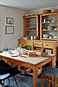Crockery on wooden kitchen table iwith shelving dresser in Cornwall cottage UK