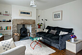 Blue belvet tw-seater sofa with wood-burning stove in living room of Cornwall cottage UK