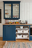Glass fronted cabinet above worktop with blue paintwork in panelled kitchen of Cornwall cottage UK