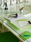 Sunglasses and bulldog clips with folder on glass-topped desk in summerhouse work studio UK