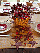 Korb mit roten Beeren und Herbstblättern mit Gedecken auf einem hölzernen Esstisch UK