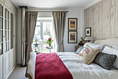 Cut flowers in window of bedroom with red blanket and framed artwork in Penzance farmhouse Cornwall UK