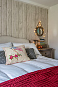 Circular mirror with fairylights above chest of drawers at bedside in Penzance farmhouse Cornwall UK