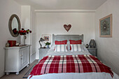 Cut flowers and circular mirror with red and white checked blanket on double bed in Penzance farmhouse Cornwall UK
