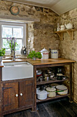 Belfast sink at farmhouse window with exposed stone wall and pans on shelf storage Helston Cornwall UK
