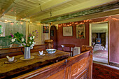 Altmodische Sitzbank und Tisch aus Holz mit Blick durch die Tür und beleuchteten Fenstern in einem Bauernhaus in Helston, Cornwall UK