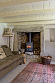 Brown sofa with floor lamp at fireside with lit woodburning stove in Helston farmhouse living room Cornwall UK