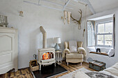 Checked armchair with lit woodburning stove in living room of Marazion beach house Cornwall UK