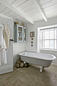 Bathrobe hangs on back of bathroom door with freestanding bath and cabinet in Marazion beach house Cornwall UK