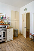 Stainless steel oven and cupboard storage in retro style London kitchen with wooden floor UK