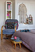 Summer dress and bags hang on wardrobe with armchair and knitting in London bedroom UK