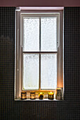 Lit candles on uncurtained windowsill in tiled London bathroom UK