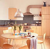 Offene Wohnküche mit hellen Holzeinbauschränken, dunkelgrauen Mosaikfliesen und einem runden Tisch mit Stühlen