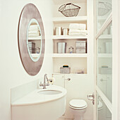 Small bathroom with built in storage decorated in white with a large round metallic mirror 
