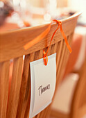 Namensschild mit Thomas, das mit einem orangefarbenen Band an die Rückenlehne eines Esszimmerstuhls gebunden ist