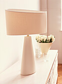 Lamp and vase of flowers on sideboard in a neutral coloured living room