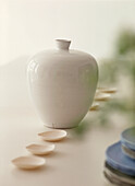 Elegante weiße Keramikvase auf dem Esstisch mit einer Reihe von kleinen Tellern an beiden Seiten