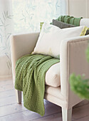 Green knitted blanket on white upholstered armchair in a white living room