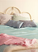Double bed in a white bedroom with colourful embroidered cushions and silk sheets in pastel shades 