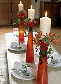Pretty winter themed table setting with tall red candlesticks and burning white candles