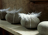 Still life of pebbles and white feathers tied with ribbon on a marble shelf