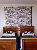 Schlafzimmer mit zwei Kiefernbetten und Indigo-Bettwäsche und Toile de Jouy-Textilwandbehang