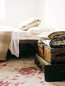 Bed in bedroom with leather trunks as table on pretty floral patterned rug