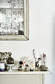 A slim mantlepiece in the kitchen displaying fairies and small objects with a foxed french mirror
