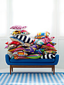 Assortment of bright cushions stacked on blue sofa with gingham fabric