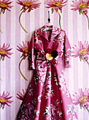 Pink vintage dress hangs against floral wallpaper