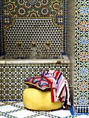 Stoffe auf einem gelben Sitz mit eingelassenem Wasserbecken in einem marokkanischen Innenhof Nordafrika