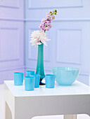 Schnittblumen in türkisfarbener Vase mit hellblauen Glaswaren auf einem Beistelltisch