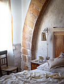 Unmade bed with stone arch and wooden chair Sicily Italy