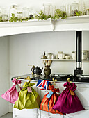 Personalisierte Geschenktüten hängen am Ofen unter einem Regal mit Gläsern und Efeu
