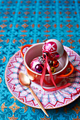 Metallic baubles in bowl on patterned plate