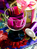 Assorted pink ribbon in wineglass with spool of thread