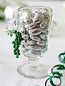 Vase of silver pebbles with green berries and streamer