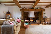 Bücherablage auf dem Kaminsims über dem beleuchteten Holzofen im Wohnzimmer des Hauses der Familie Cranbrook, Kent, England, UK