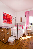 Metal framed bed with red floral artwork in bedroom with wooden floorboards, Manchester family home, England, UK